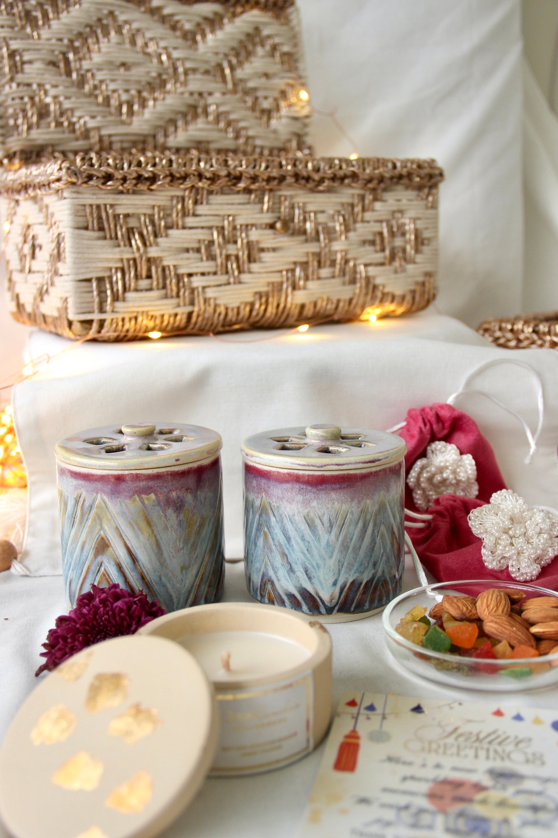 Decorative scene with candles, a woven basket, and small items on a white surface.